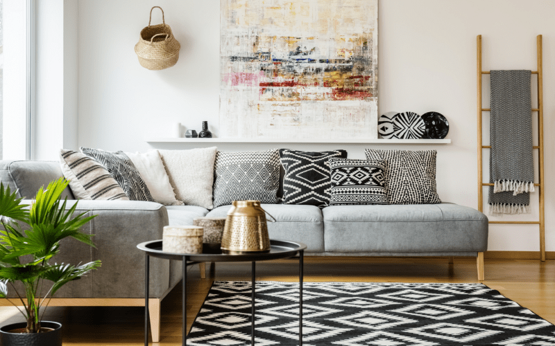 Patterned pillows on grey corner sofa in living room interior with table and painting