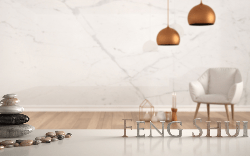 White table shelf with pebble balance and 3d letters making the word feng shui over empty room with marble wall, white armchair, candles and decor, zen concept interior design, 3d illustration