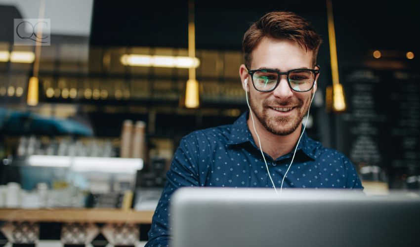 Businessman sitting in a restaurant listening to music while working on a laptop. Smiling man wearing earphones managing business work on laptop sitting in a cafe.