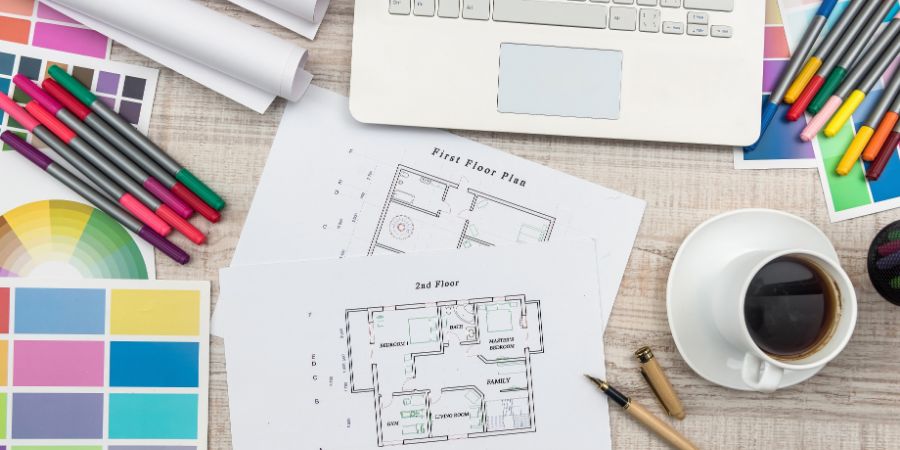 Designer's workplace top view. House plan with colorful palettes, laptop and cup of coffee. QC Design School article.