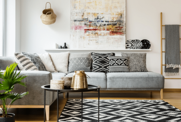 Patterned pillows on grey corner sofa in living room interior with table and painting