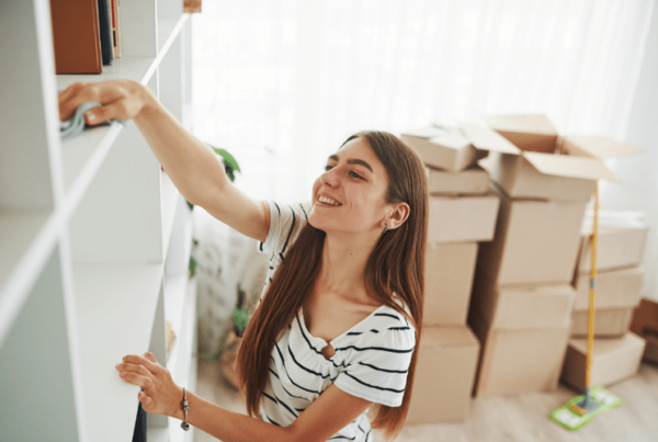 female pro organizer wiping down shelf with cloth, with packing boxes behind her