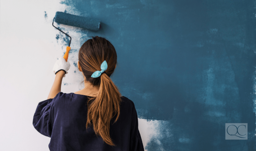 woman using roller to paint a wall a dark turquoise