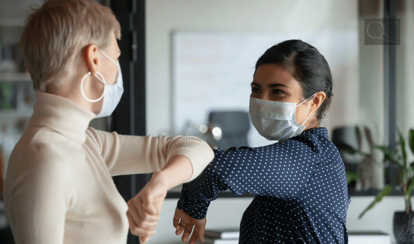 two women wearing face masks and bumping elbows to say hello