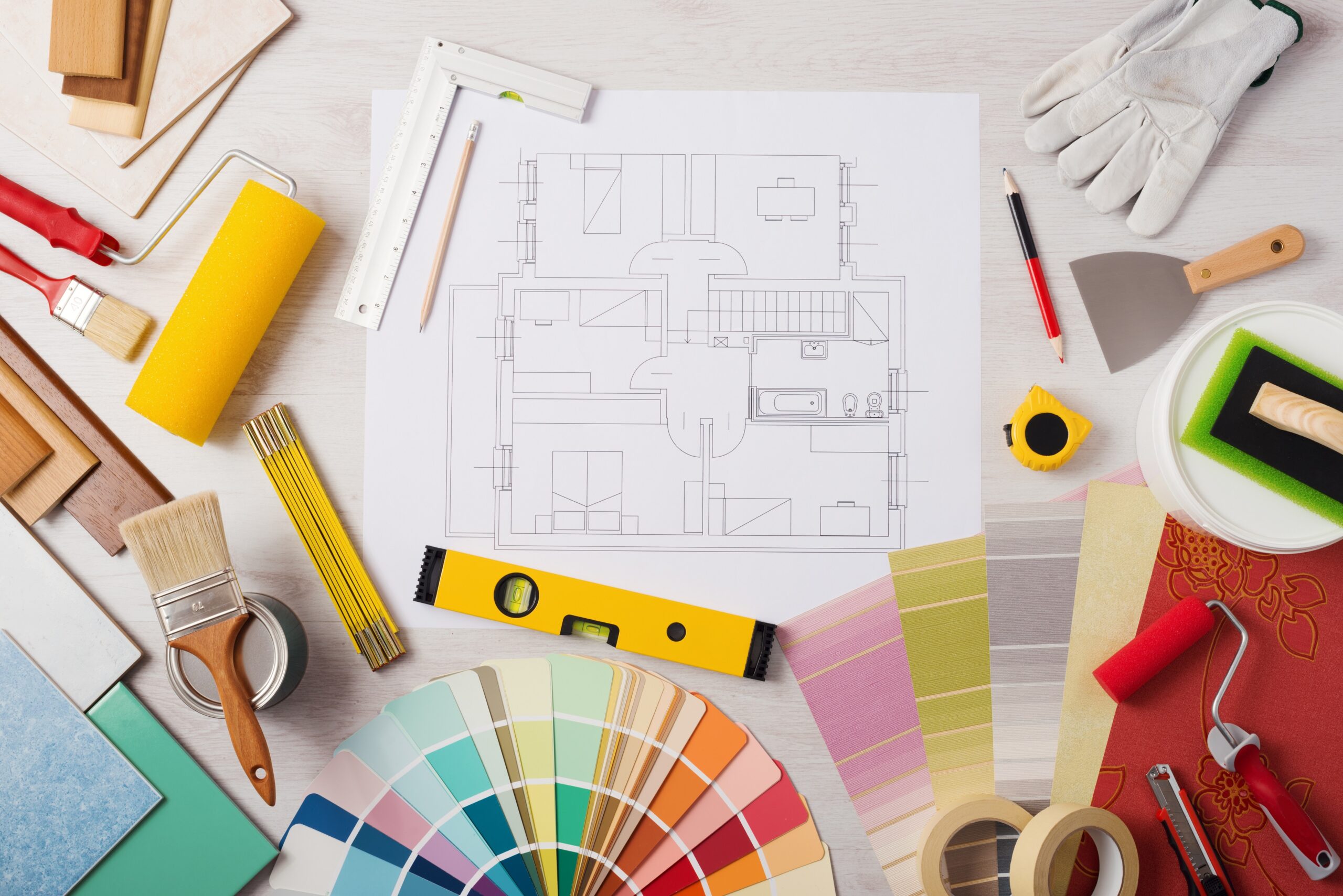 Decorator work table with house project, paint brush and painting roller, color swatches and tools, top view