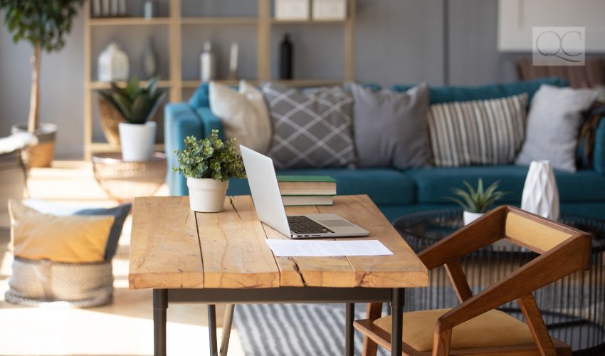 Sunlight illuminates living room workplace home office interior for comfort productive work, brown and blue colours. On wooden table laptop comfy couch with cushions on background, workday end concept