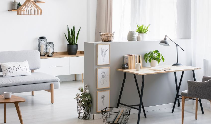 Grey armchair at desk with plant and lamp in flat interior with wooden table next to couch. Real photo