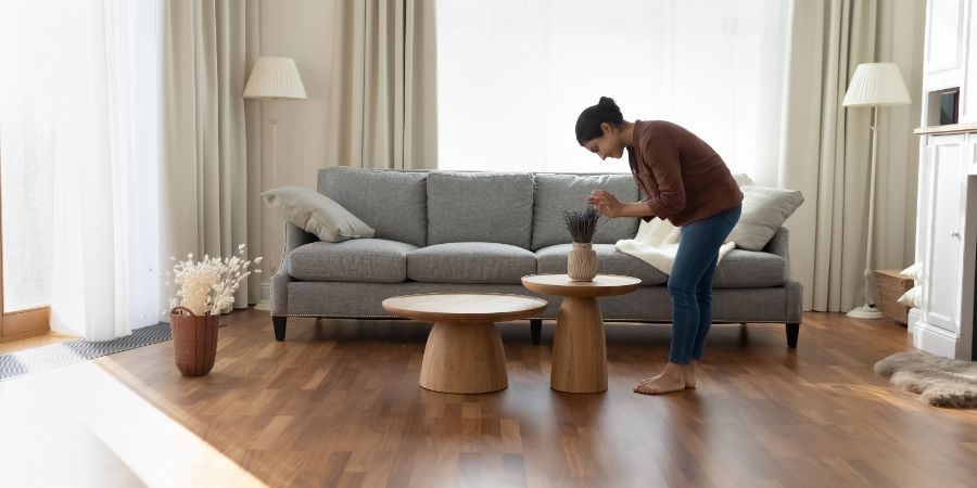 Full length of young woman standing in modern spacious living room create cosiness at home, arranging flowers bunch in vase. Housework routine, interior designer workflow. Design article.