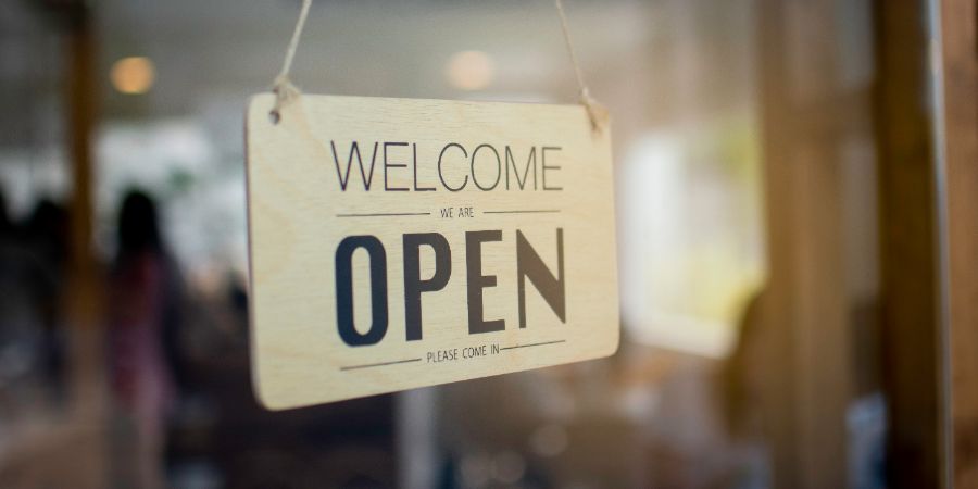 A wooden sign hanging in front of a mirror at the entrance of the coffee shop Concept of opening shop in the morning. Home design business money article.